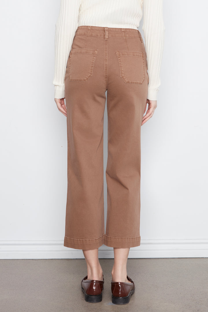 A person shown from the back wearing tan cropped wide-leg pants with back patch pockets, a cream ribbed sweater, and dark brown loafers, standing against a plain white wall.