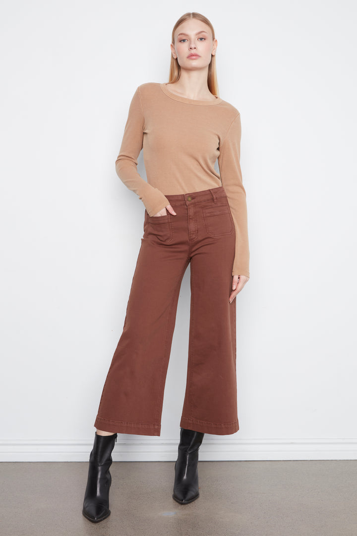 A woman modeling a tan long-sleeve knit top and rust-brown wide-leg cropped pants with black ankle boots, standing against a plain white wall.