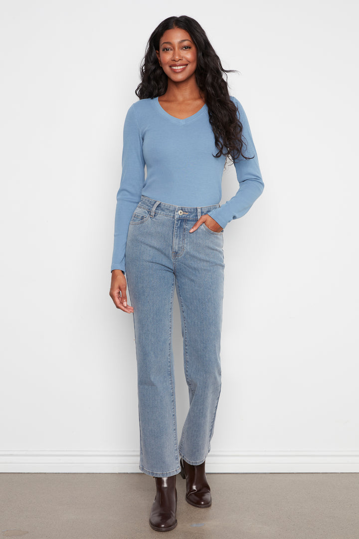 A woman modeling a light blue long-sleeve knit top and light-wash blue straight-leg jeans, standing against a plain white wall.
