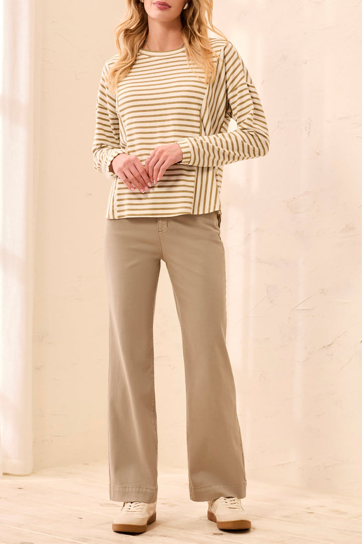 A woman modeling a beige and white striped long-sleeve top with beige wide-leg pants and white sneakers, standing in a bright indoor setting.