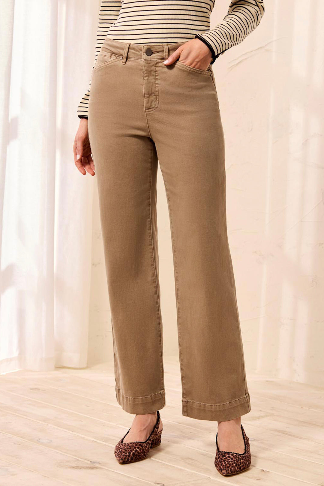 A woman modeling a beige and white striped long-sleeve top with brown wide-leg pants, standing in a bright indoor setting.