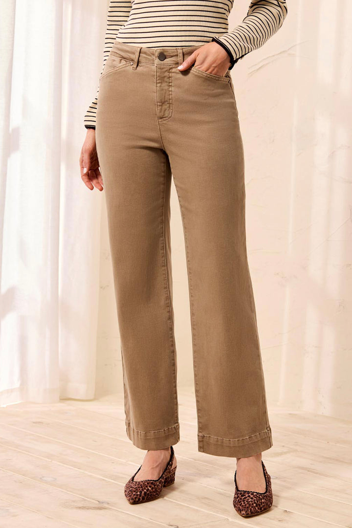 A woman modeling a beige and white striped long-sleeve top with brown wide-leg pants, standing in a bright indoor setting.