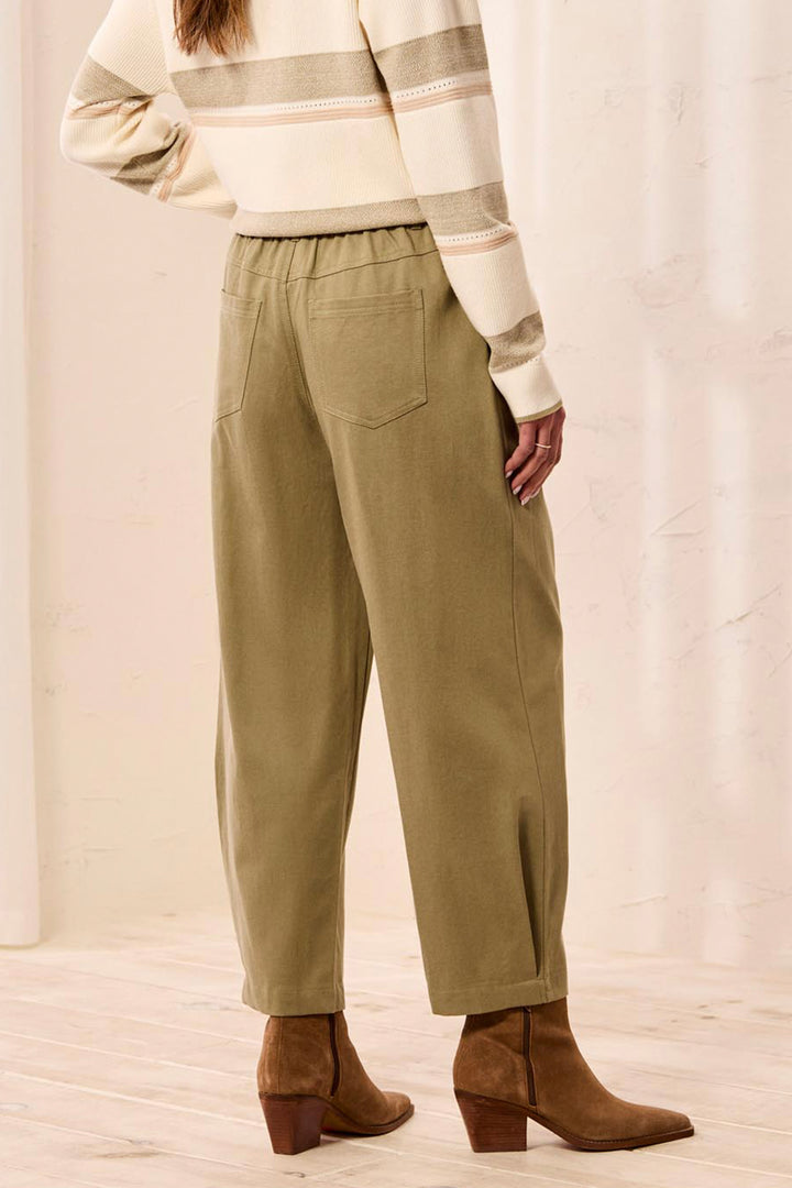 A person shown from the back wearing wide-leg olive green pants, a cream and beige striped sweater, and brown ankle boots in a softly lit indoor setting.