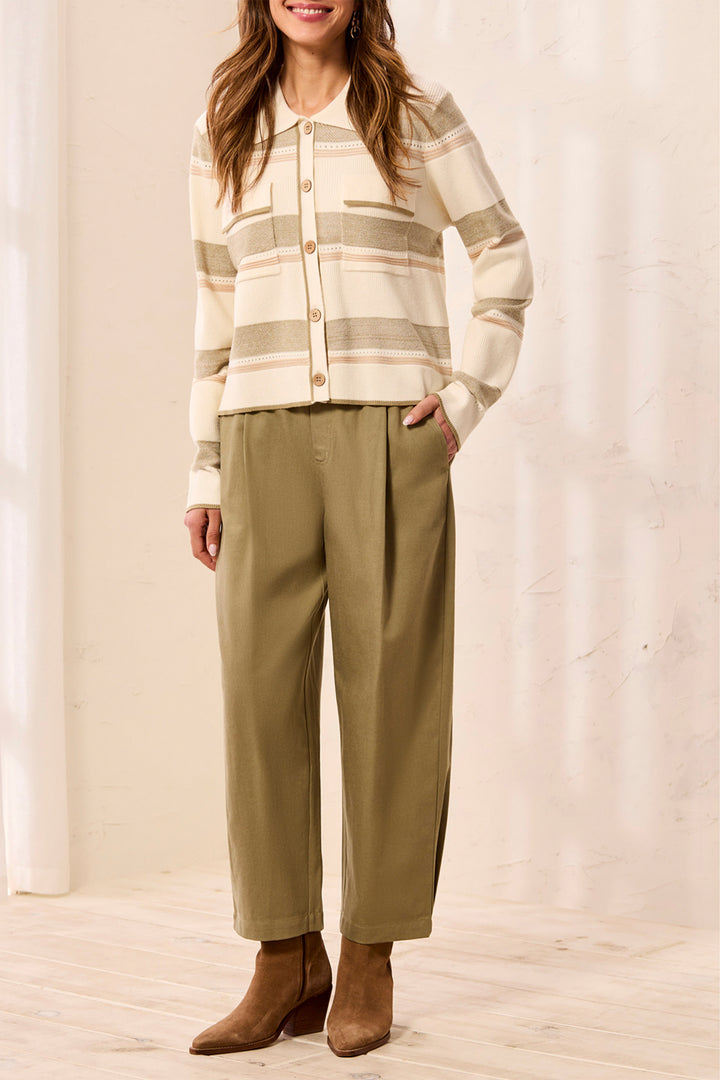 A woman models a cream and beige striped knit cardigan with brown buttons, paired with olive green wide-leg cropped pants and brown ankle boots, set against a warm, softly lit studio backdrop.
