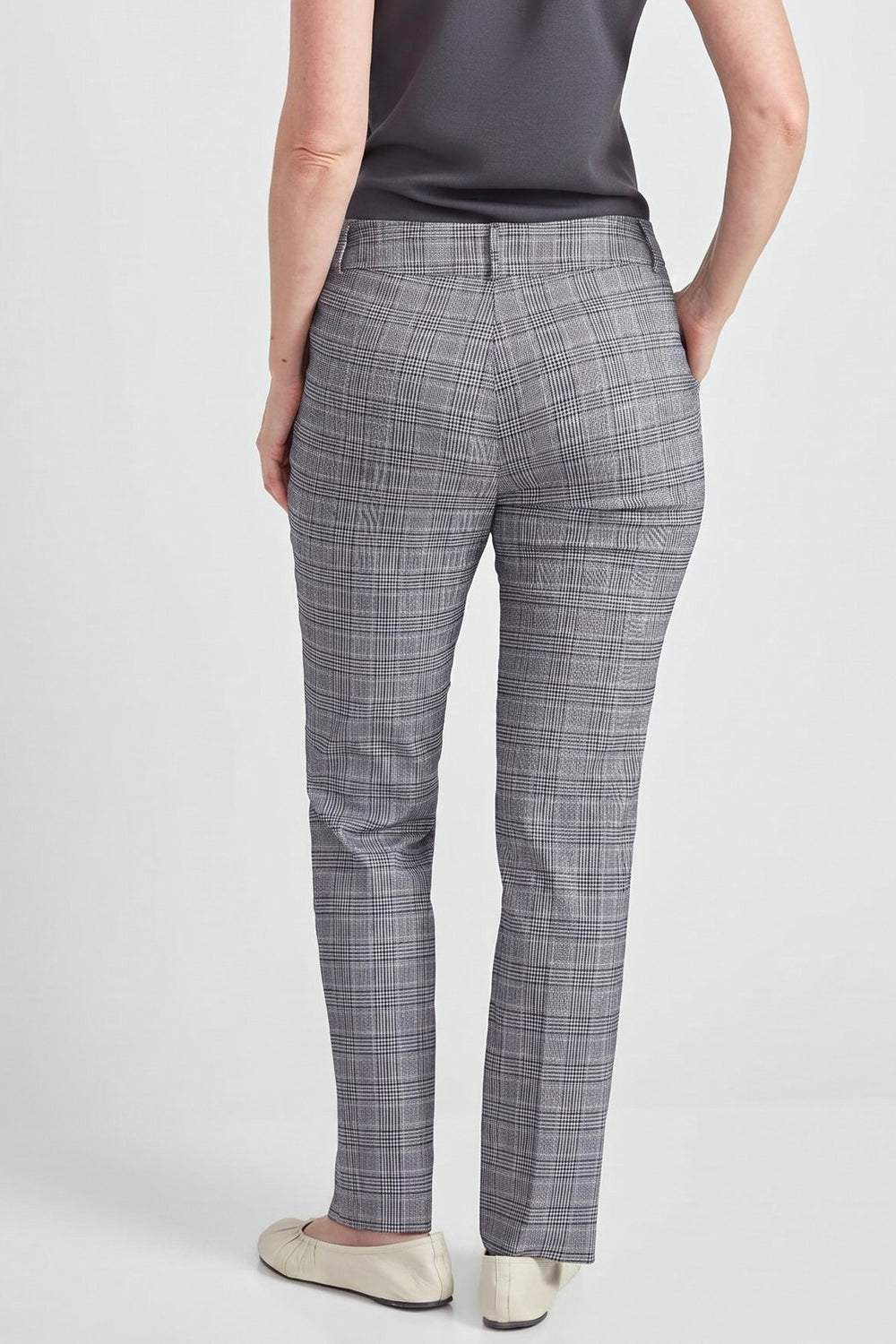 A person shown from the back wearing gray plaid trousers, a dark gray sleeveless top, and light beige flats against a light gray studio background.