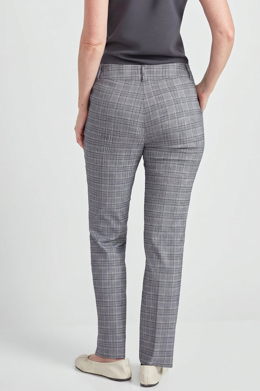 A person shown from the back wearing gray plaid trousers, a dark gray sleeveless top, and light beige flats against a light gray studio background.
