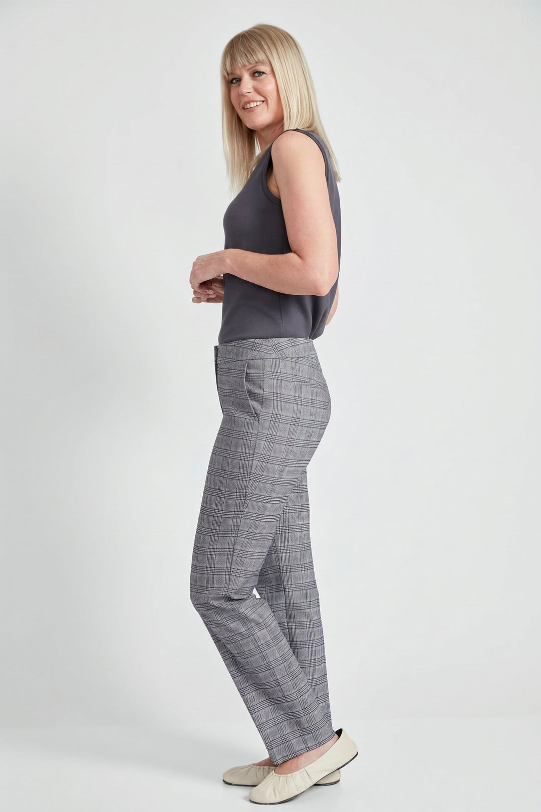 A woman modeling gray plaid trousers and a dark gray sleeveless top against a light gray studio background.