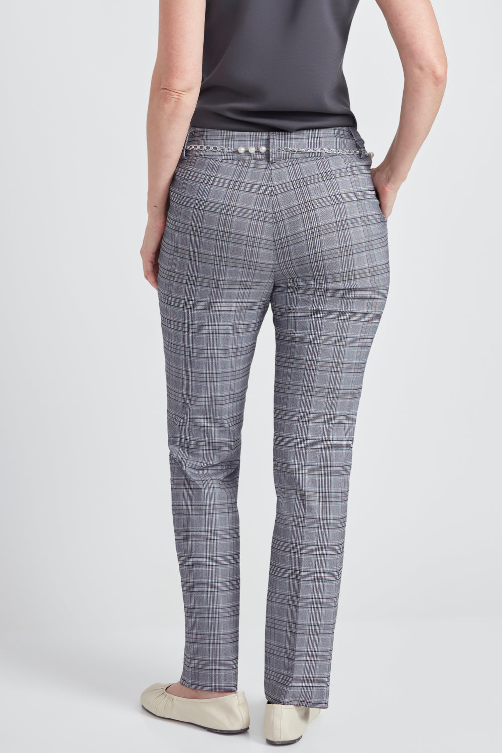 A person shown from the back wearing gray plaid trousers, a dark gray top, and beige flats against a light gray studio background.