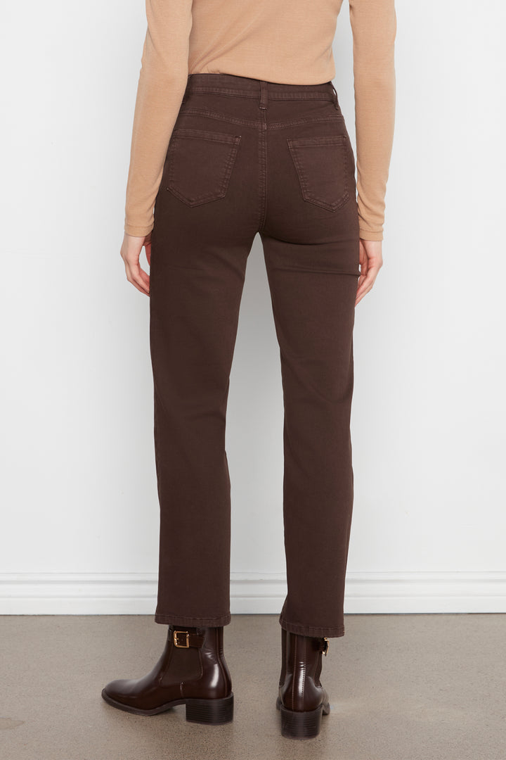 Rear view of a model wearing dark brown straight-leg jeans, a beige long-sleeve top, and dark brown leather ankle boots against a white wall.