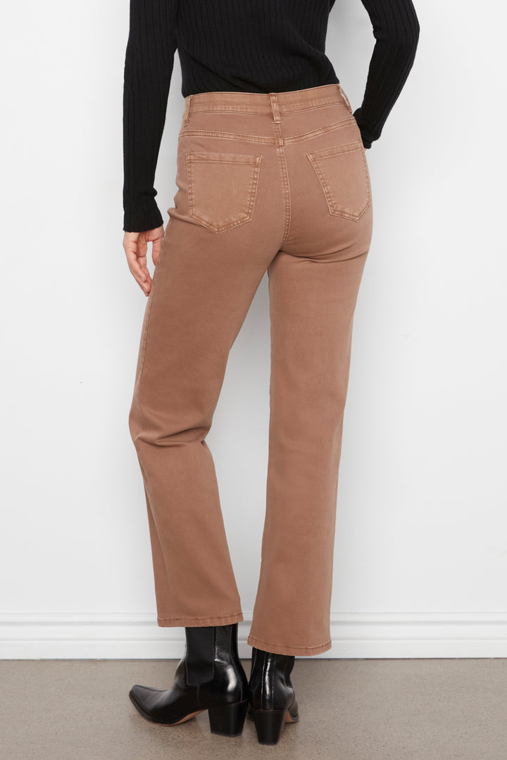A person shown from the back wearing straight-leg brown jeans, a black ribbed long-sleeve top, and black ankle boots against a white wall.