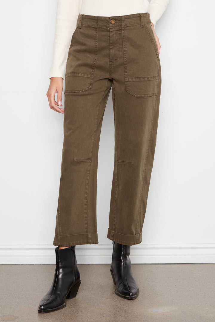 A person wearing olive brown cropped cargo pants with a cream long-sleeve top and black ankle boots, standing against a white wall.