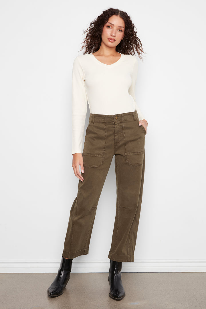 A woman modeling a cream long-sleeve knit top and olive green cropped pants with black ankle boots, standing against a white wall.