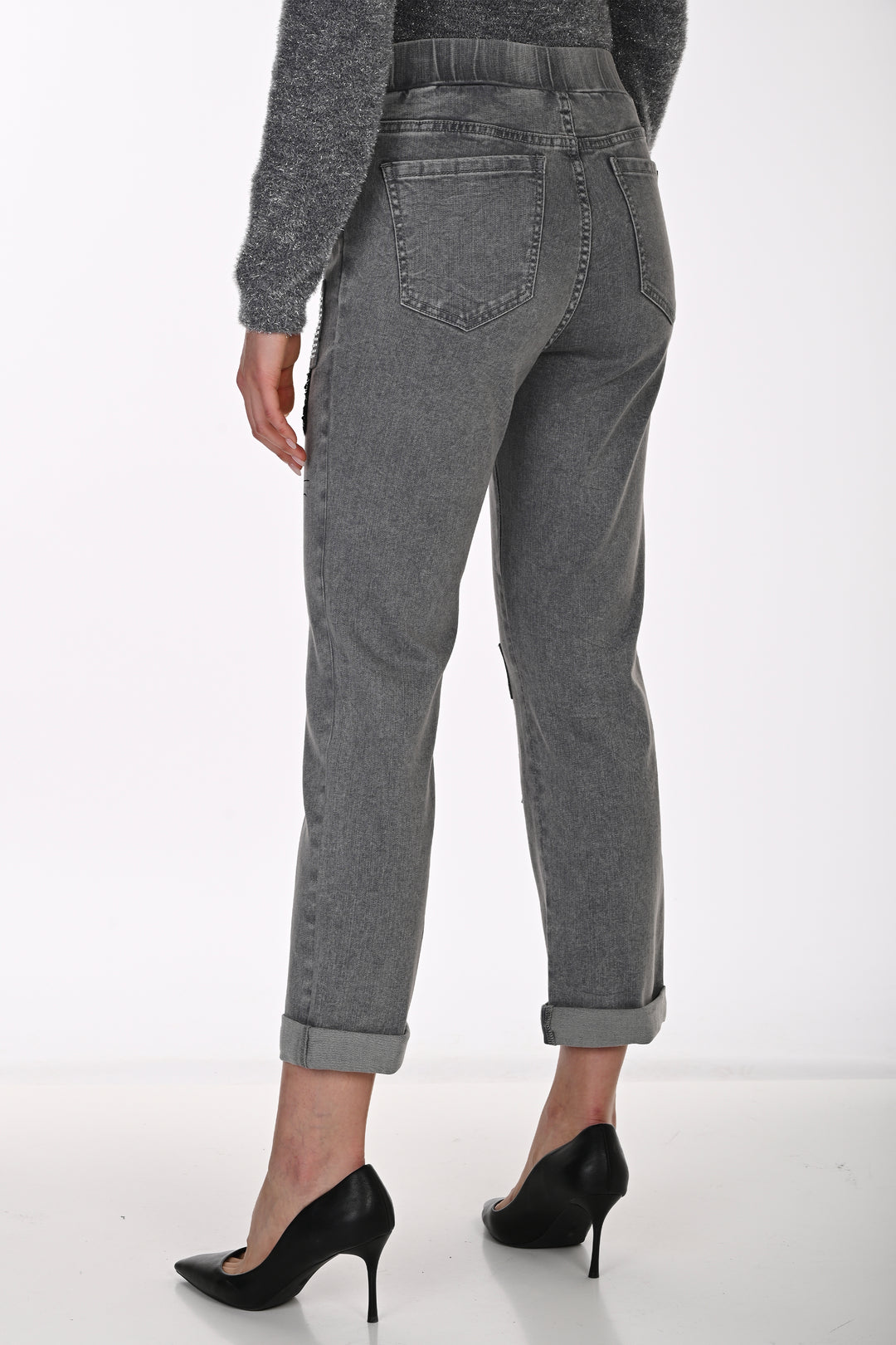 A person shown from the back wearing gray high-waisted cropped jeans with rolled cuffs and black pointed-toe heels against a clean white studio background.