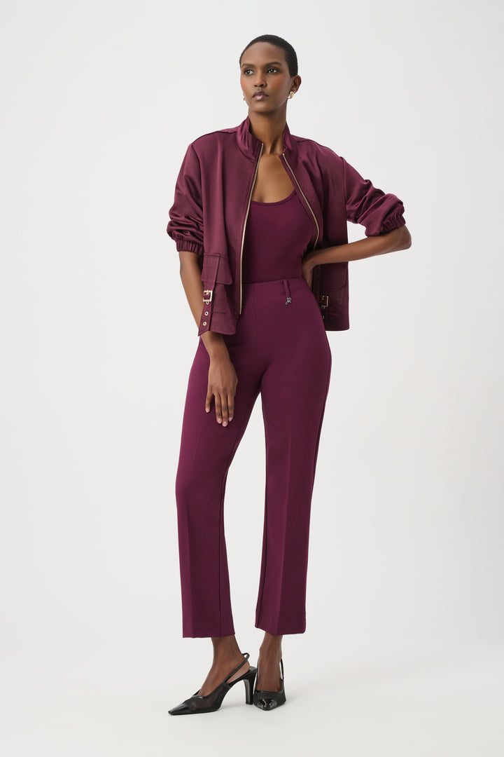 A model wearing a matching burgundy three-piece set consisting of a bomber jacket, a scoop-neck top, and cropped trousers, paired with black pointed-toe heels against a plain white studio background.