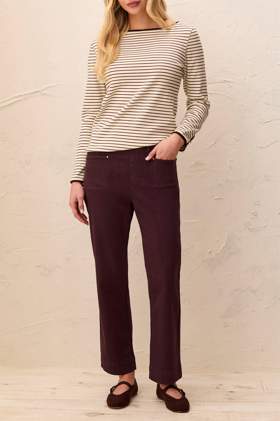 Woman wearing a striped sweater and dark pants against a plain background