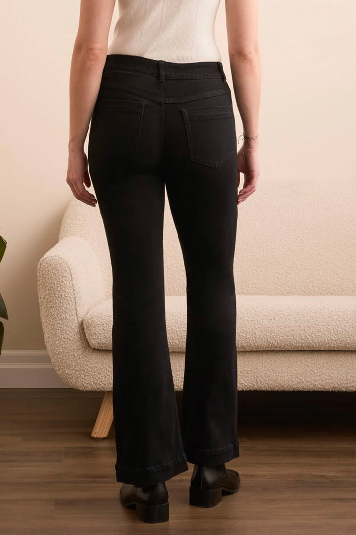 A person shown from the back wearing black flared jeans, standing in a room with a cream boucle sofa and wood floor.