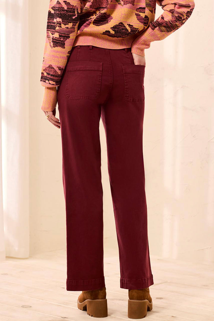 A person shown from the back wearing burgundy straight-leg pants, a pink and brown patterned sweater, and brown block-heel mules in a bright indoor setting.