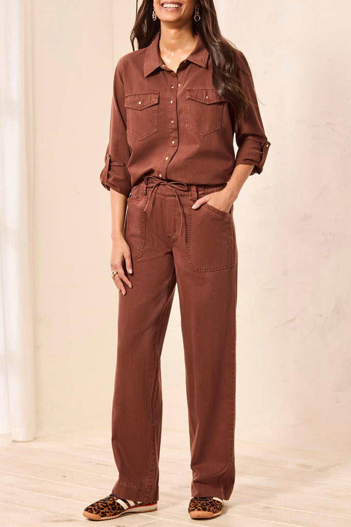 A woman wearing a matching rust-brown two-piece set consisting of a long-sleeve button-up shirt and high-waisted drawstring pants, paired with leopard-print flat shoes.