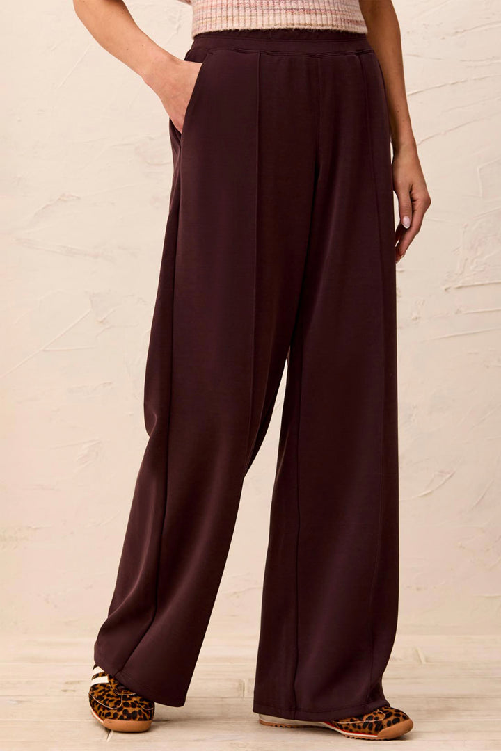 A person wearing dark plum wide-leg pants with a textured cream top and leopard-print shoes, standing against a light textured wall.