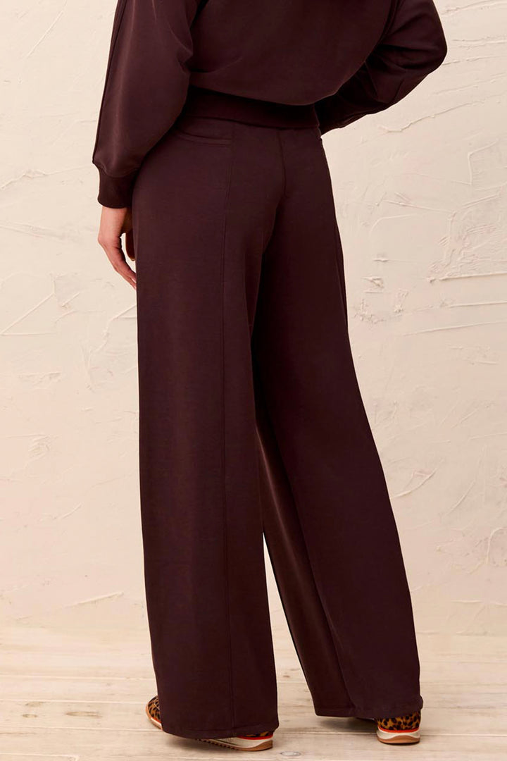 A person shown from the back wearing dark plum wide-leg pants and a matching dark plum long-sleeve top, standing against a light textured wall.