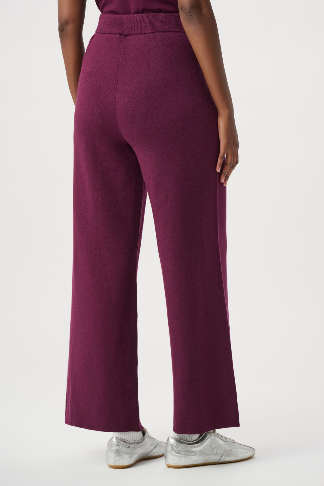 Woman wearing burgundy knit pants shown from the back on a white background