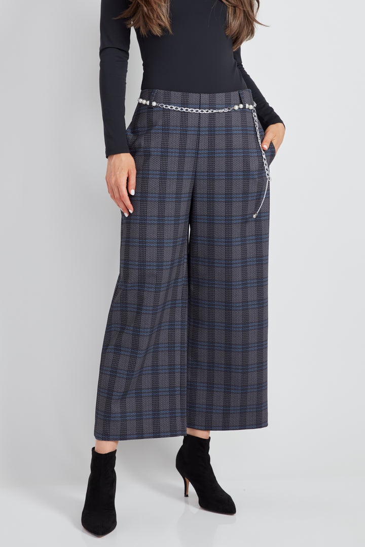 A woman standing in front of a light grey background wearing a long sleeve top with plaid wide leg crop pants.  