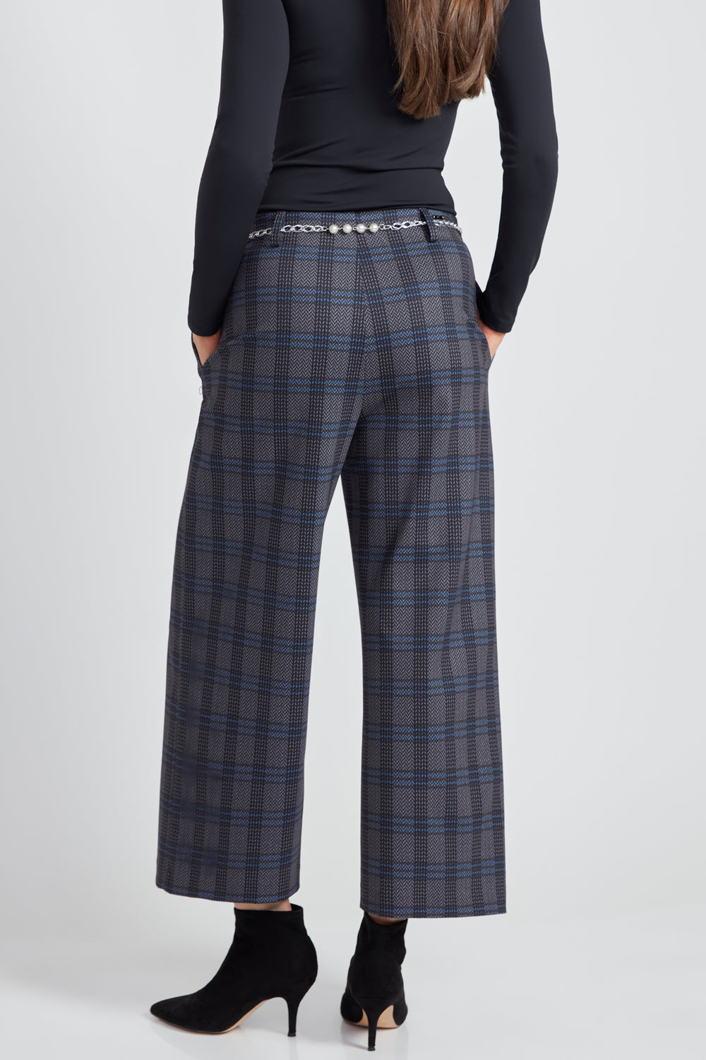 A woman standing in front of a light grey background wearing a long sleeve top with plaid wide leg crop pants.  