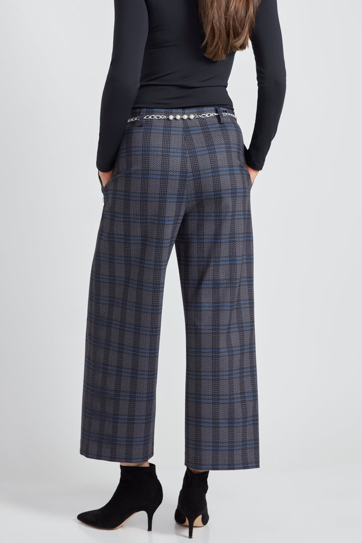 A woman standing in front of a light grey background wearing a long sleeve top with plaid wide leg crop pants.  