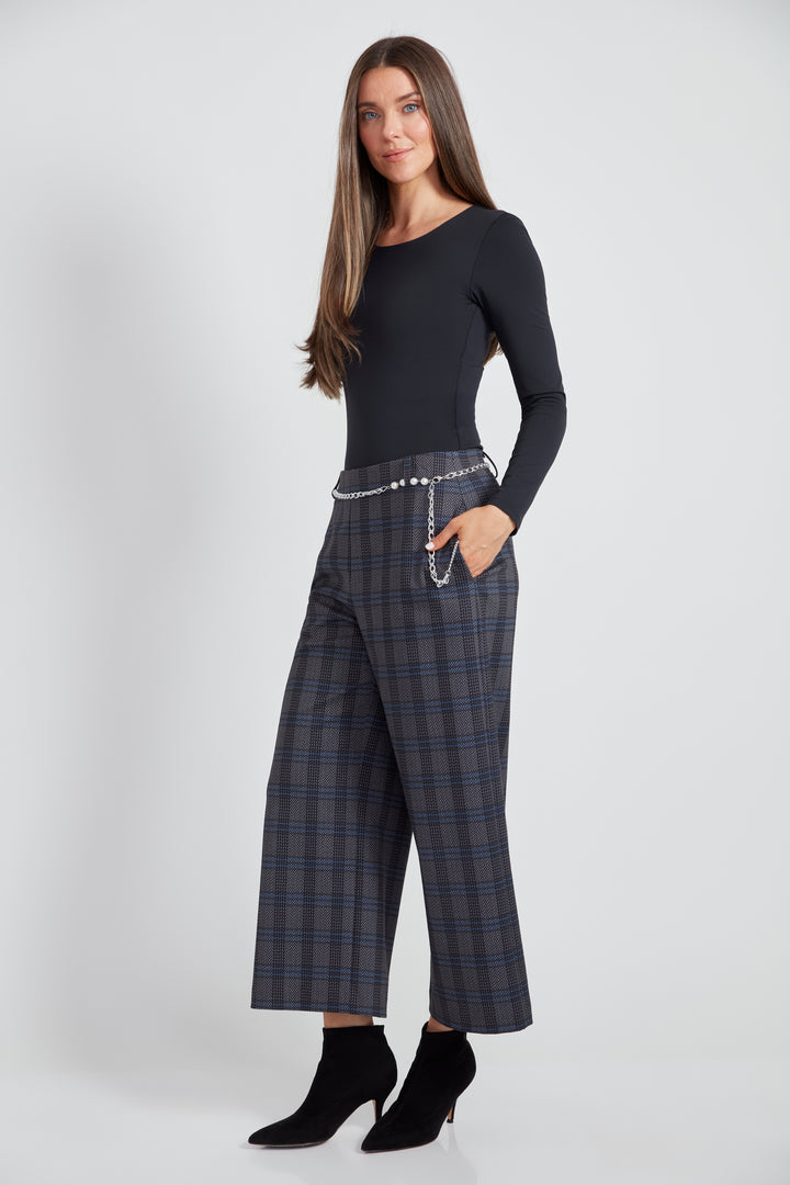 A woman standing in front of a light grey background wearing a long sleeve top with plaid wide leg crop pants.  
