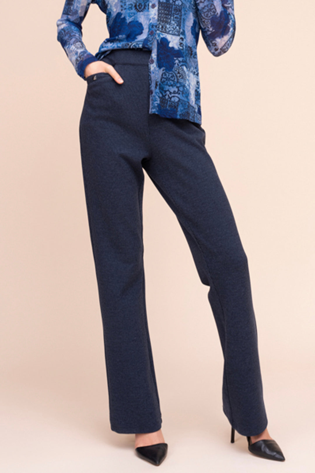 A woman modelling navy pants in front of a beige background. 