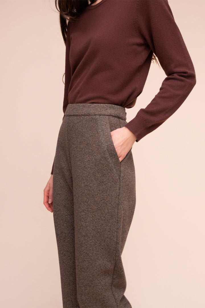 A woman modelling brown pants in front of a beige background. 