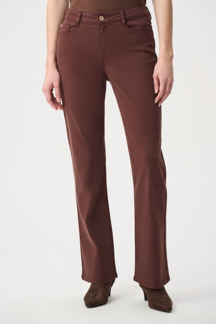 A woman wearing brown straight leg jeans standing in front of a light grey background. 