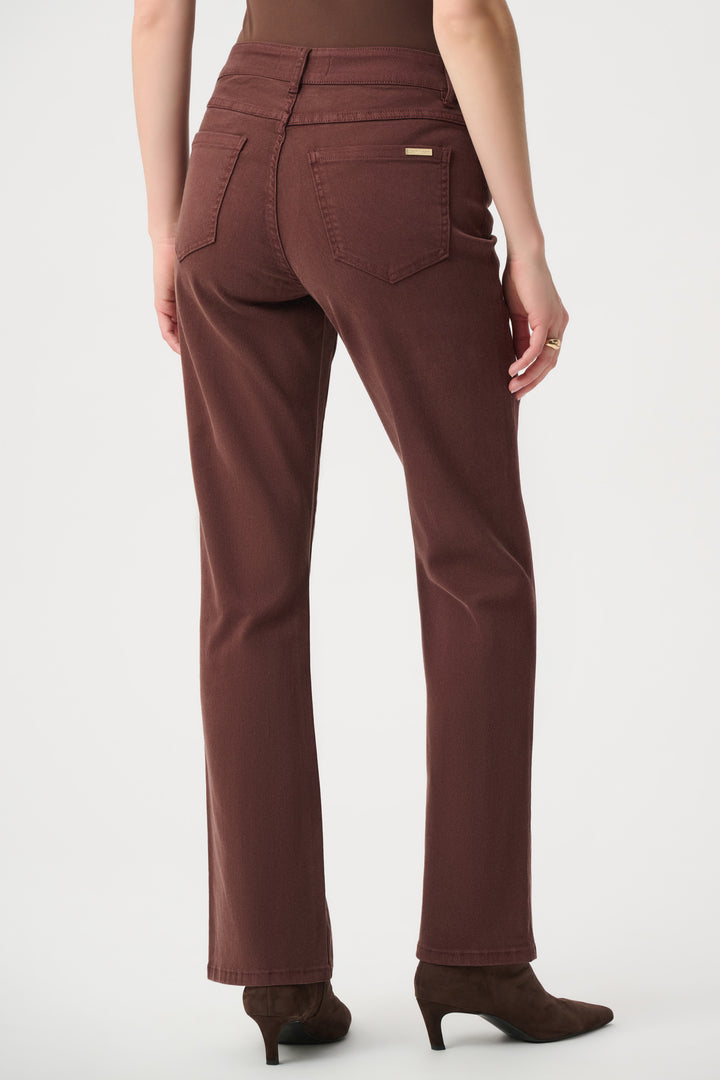 A woman shown from the back wearing brown straight leg jeans standing in front of a light grey background. 