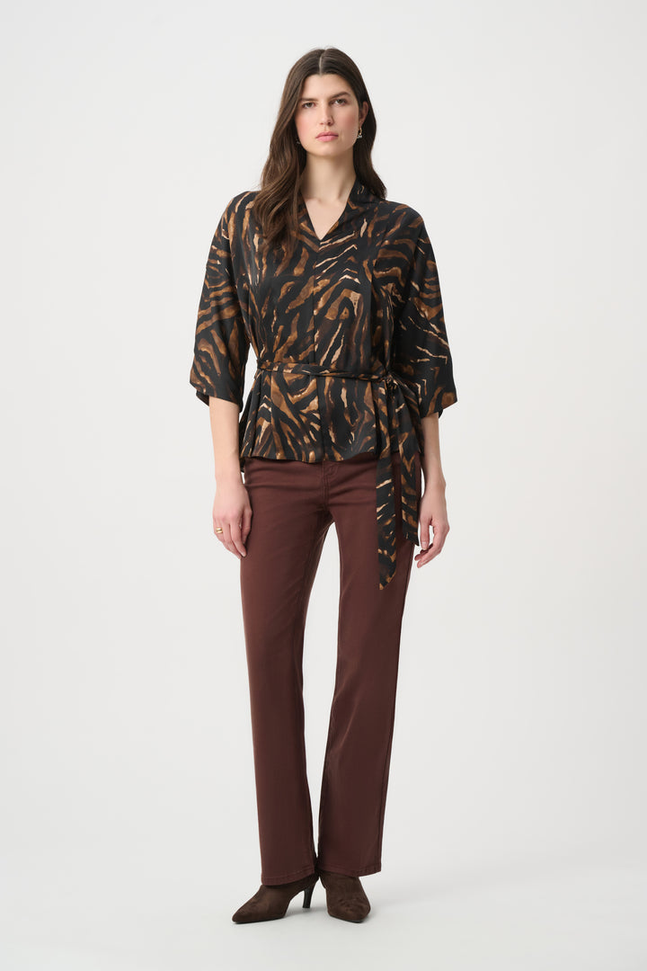A woman wearing an animal print blouse and brown straight leg jeans standing in front of a light grey background. 