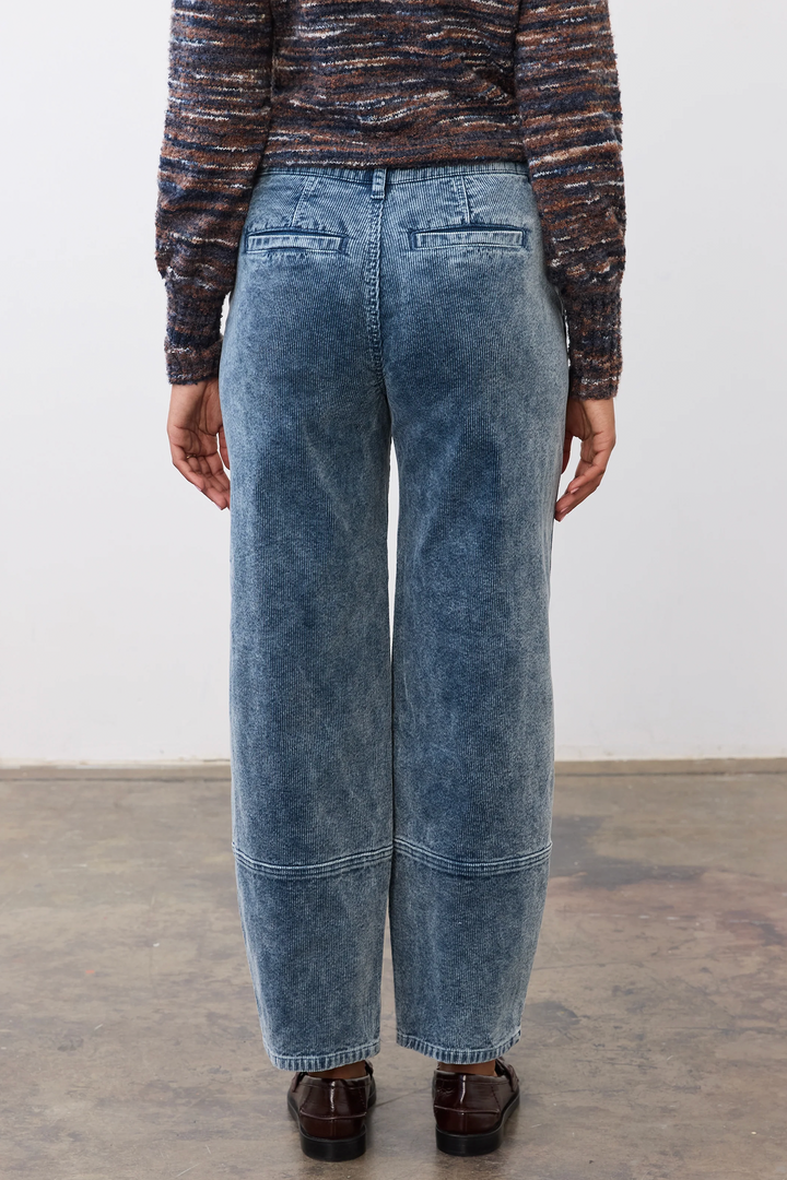 A woman shown from the back wearing a bulky sweater and light wash corduroy barrel jeans standing in front of a grey studio background. 