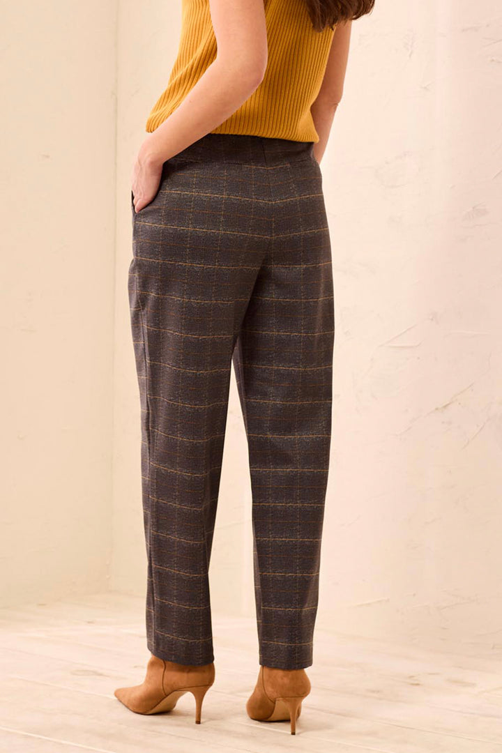 A woman shown from the back wearing brown plaid trousers standing in front of a beige background. 