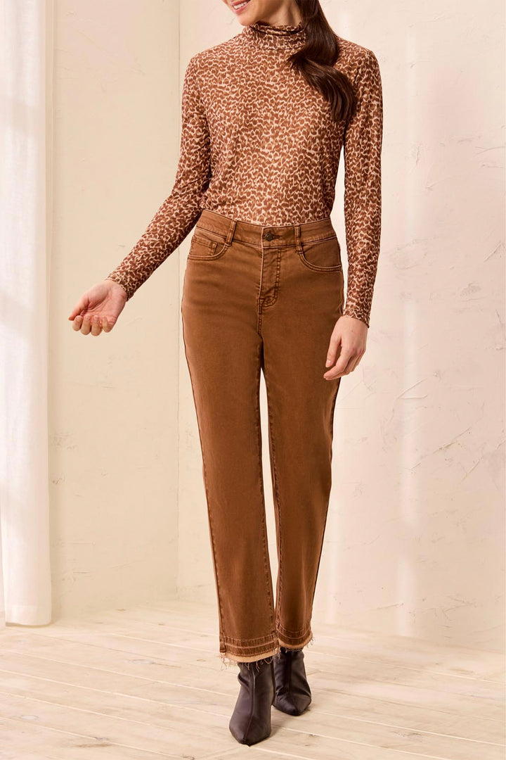 A woman wearing tan pants and brown boots standing in front of a beige background. 