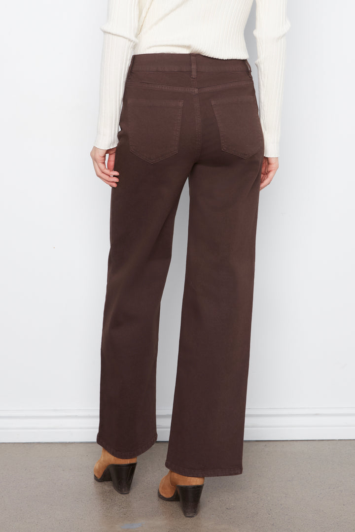 A woman shown from the back wearing brown wide leg jeans with daisy embroidery standing in front of a grey wall. 