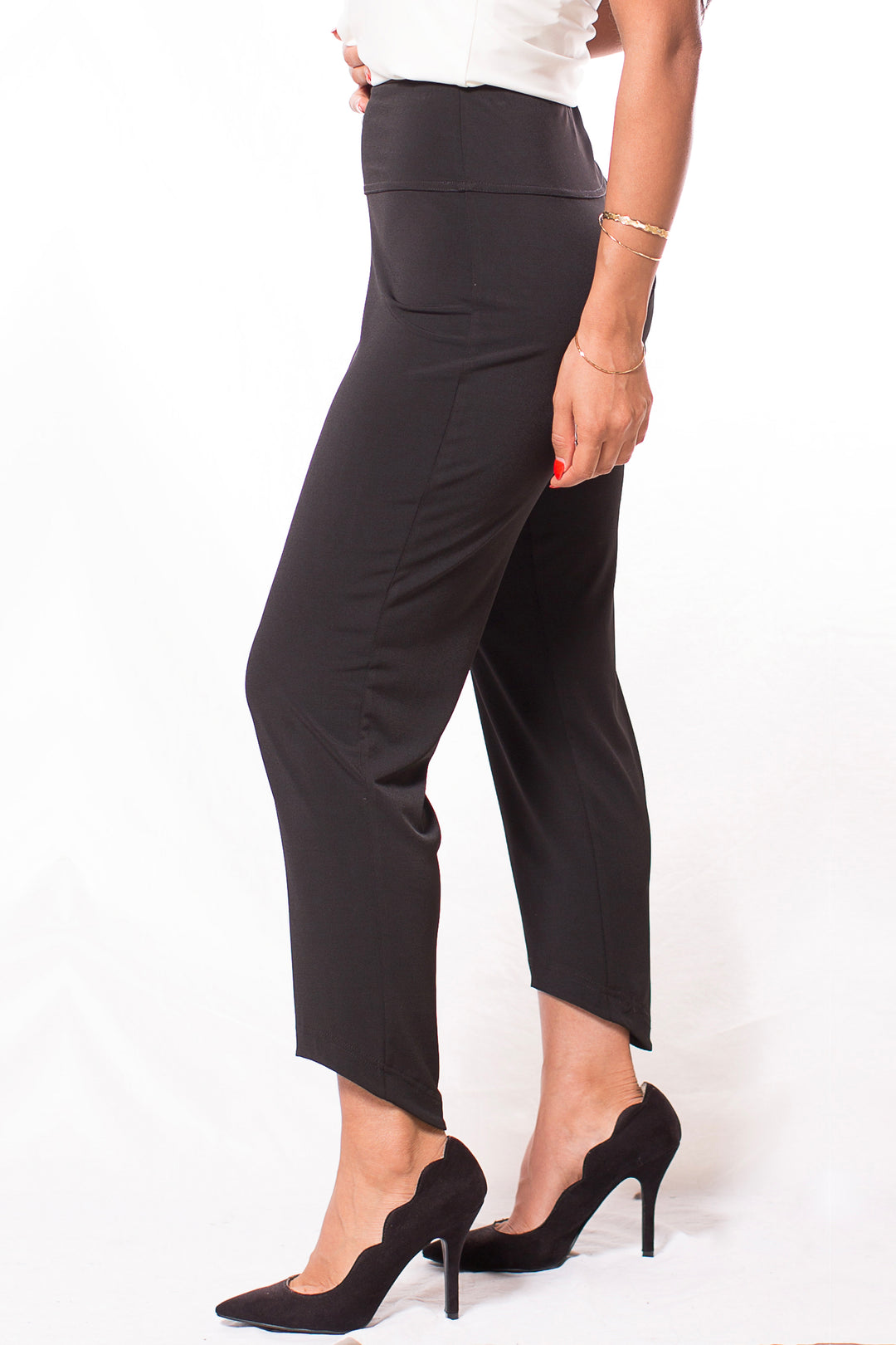 A woman modelling black pants with a high-low hem standing in front of a white background. 