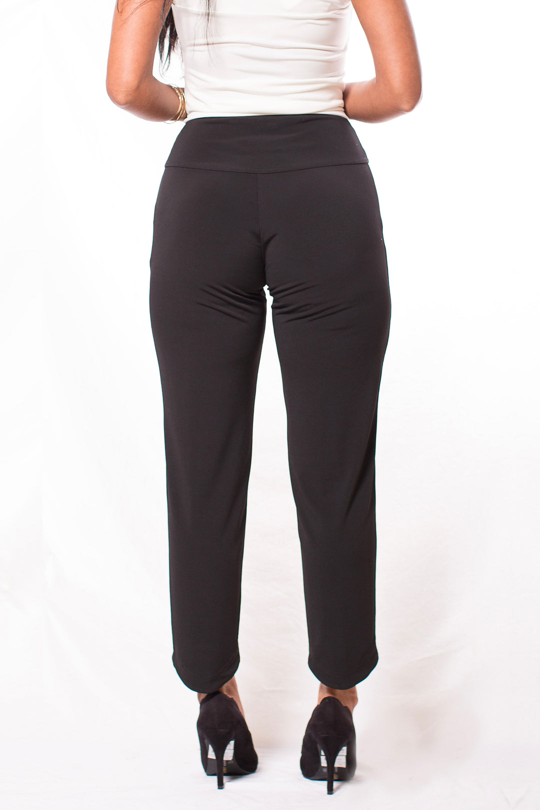 A woman shown from the back modelling black pants with a high-low hem standing in front of a white background. 