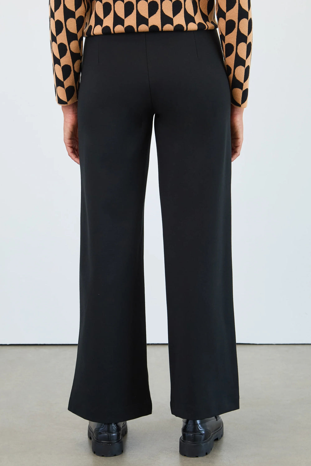 Person wearing black wide-leg pants with a patterned top against a white background