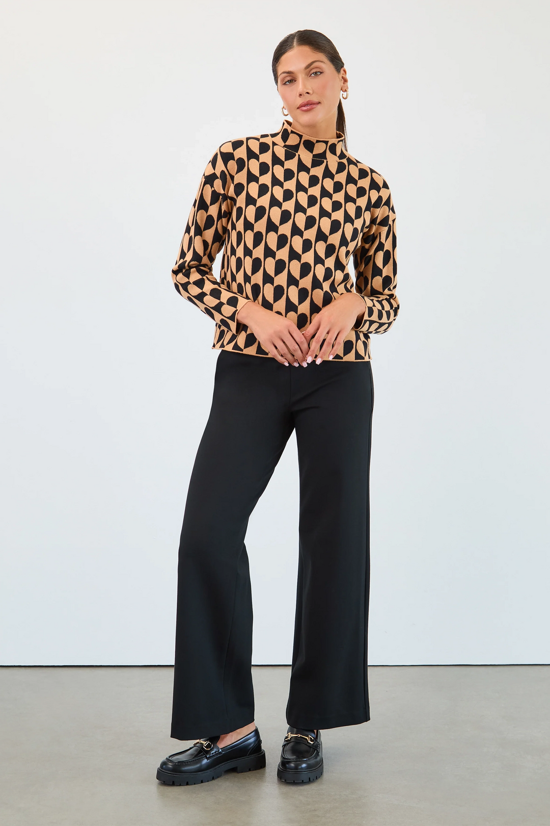 Woman wearing a patterned blouse and black pants against a white background