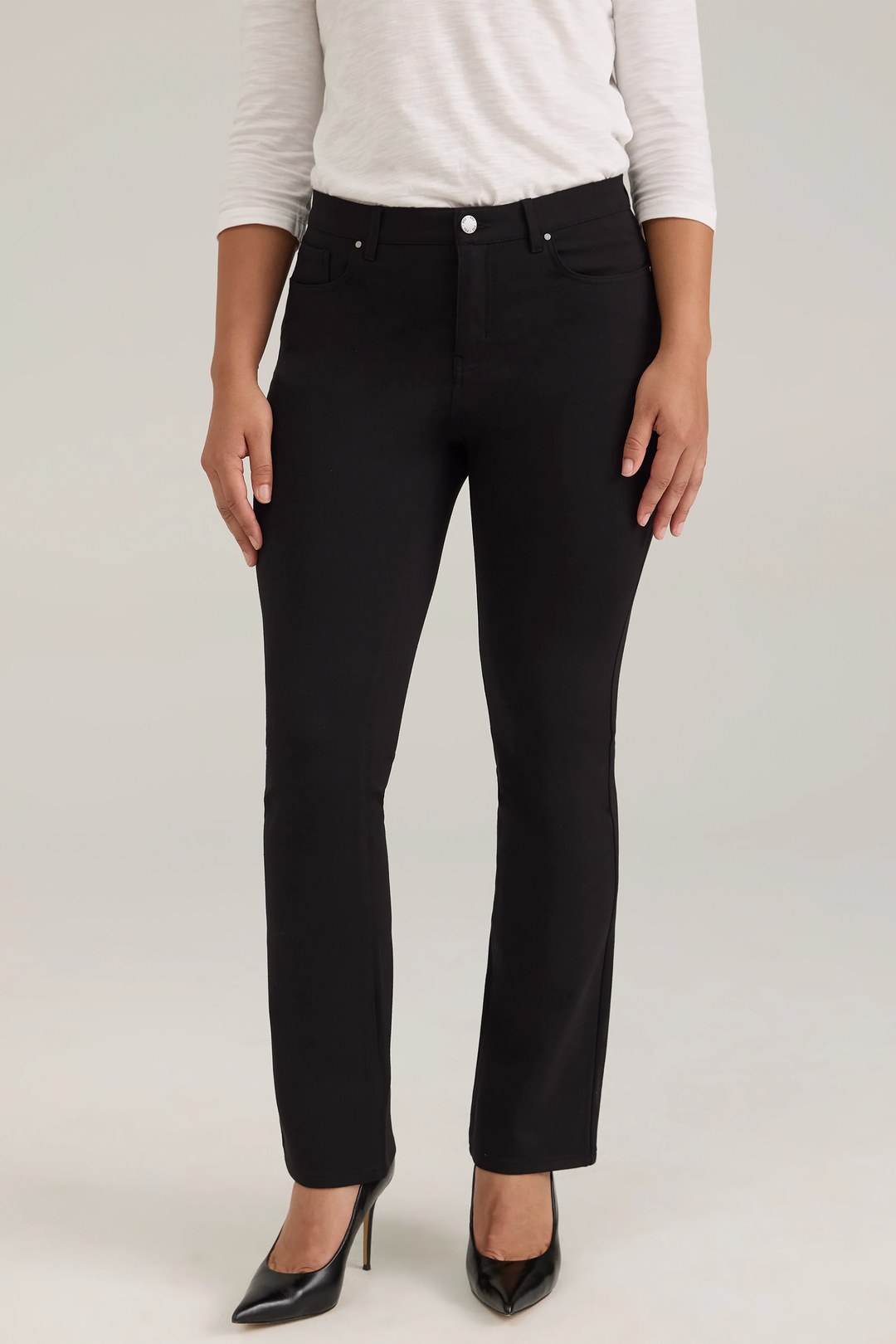 A woman modelling a long sleeve top and black jeans against a light grey background. 