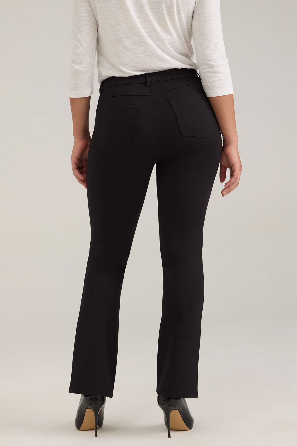 A woman modelling a long sleeve top and black jeans against a light grey background. 
