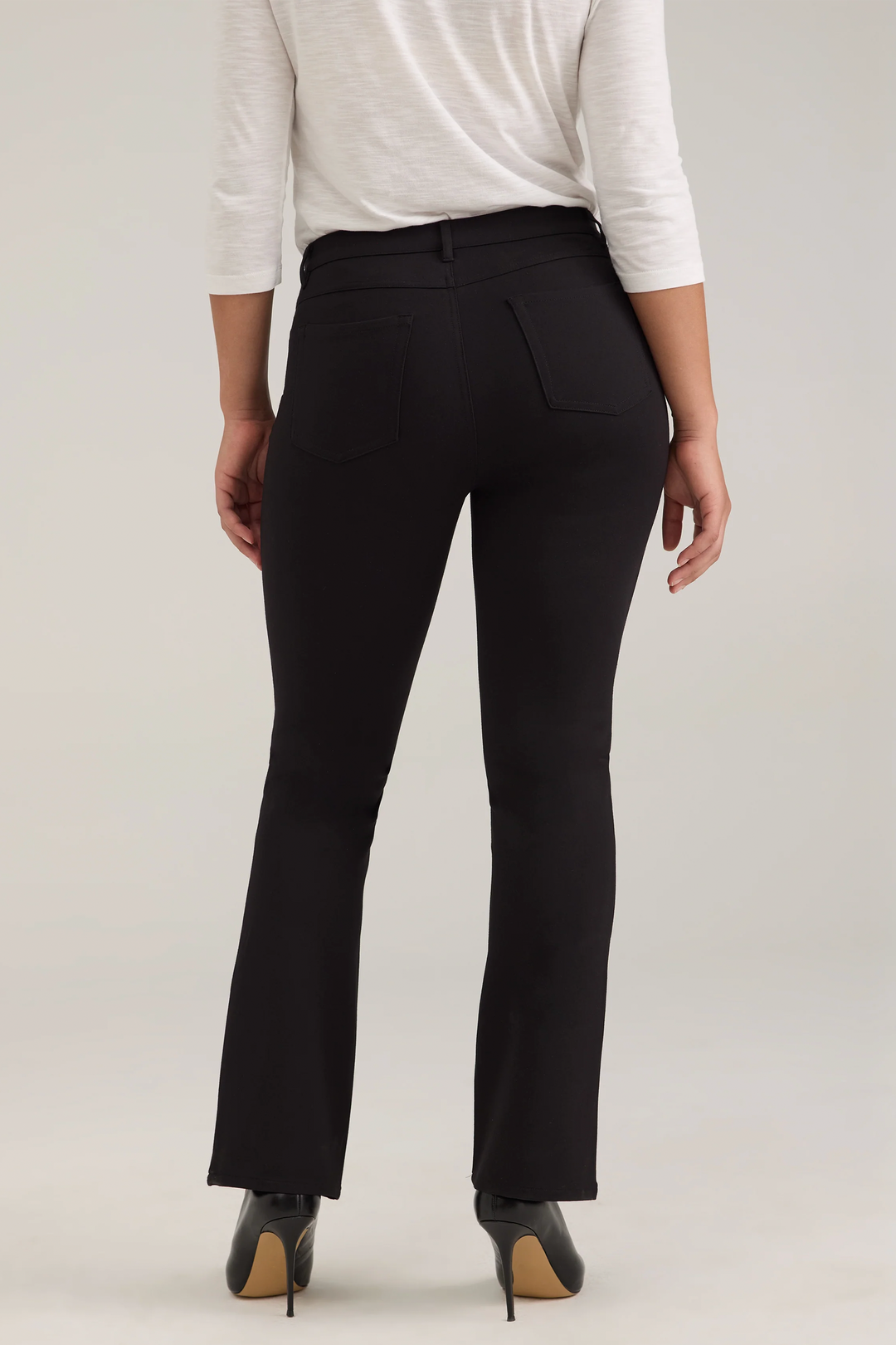A woman modelling a long sleeve top and black jeans against a light grey background. 