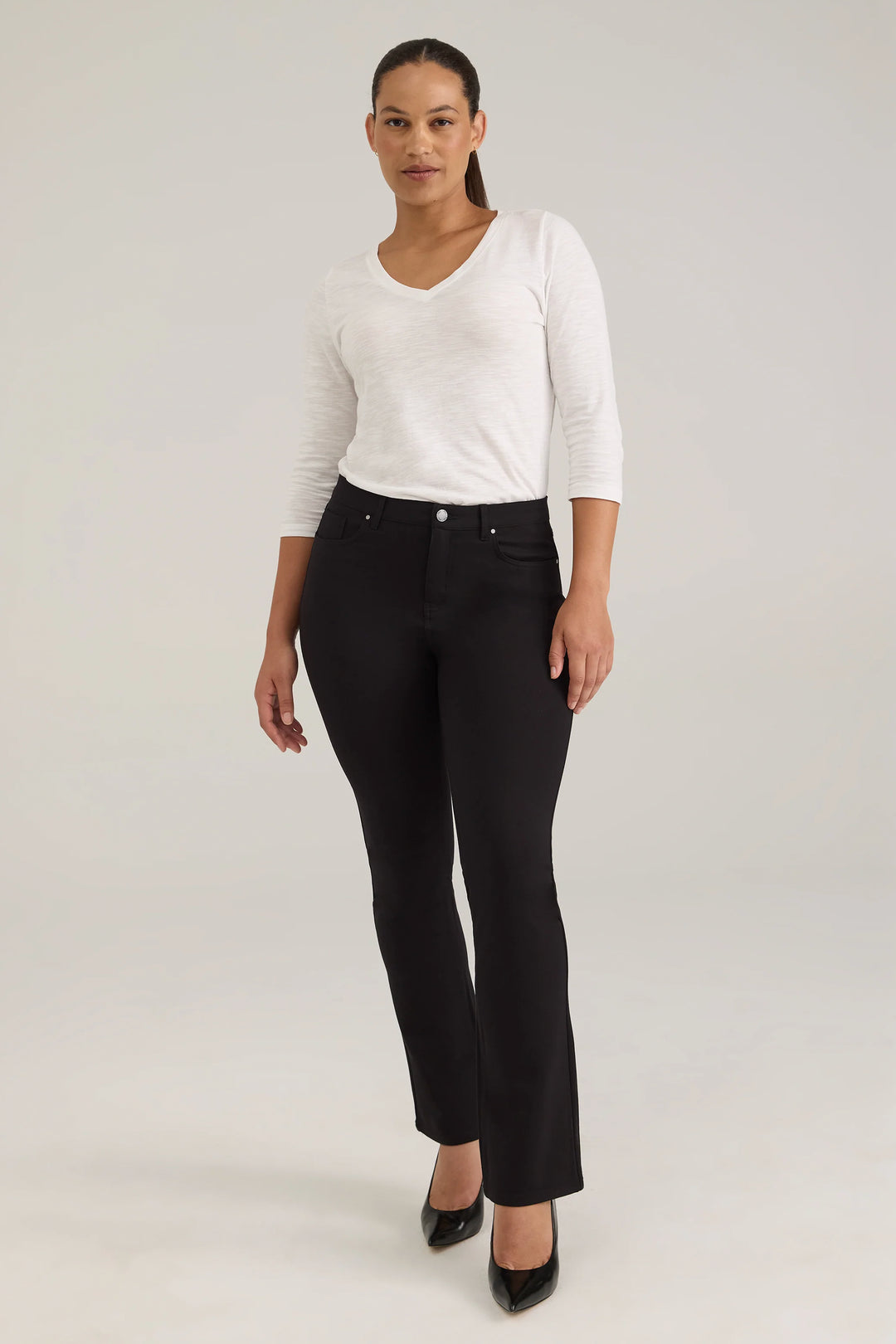 A woman modelling a long sleeve top and black jeans against a light grey background. 