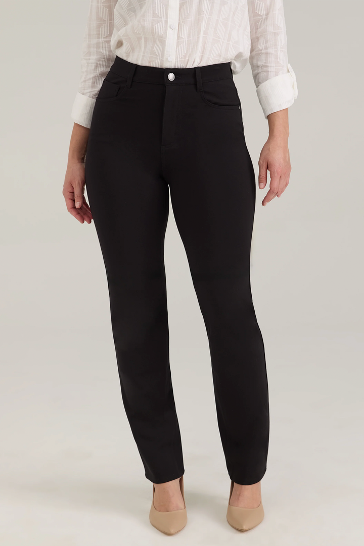 A woman modelling a white blouse and black pants standing in front of a light beige background. 