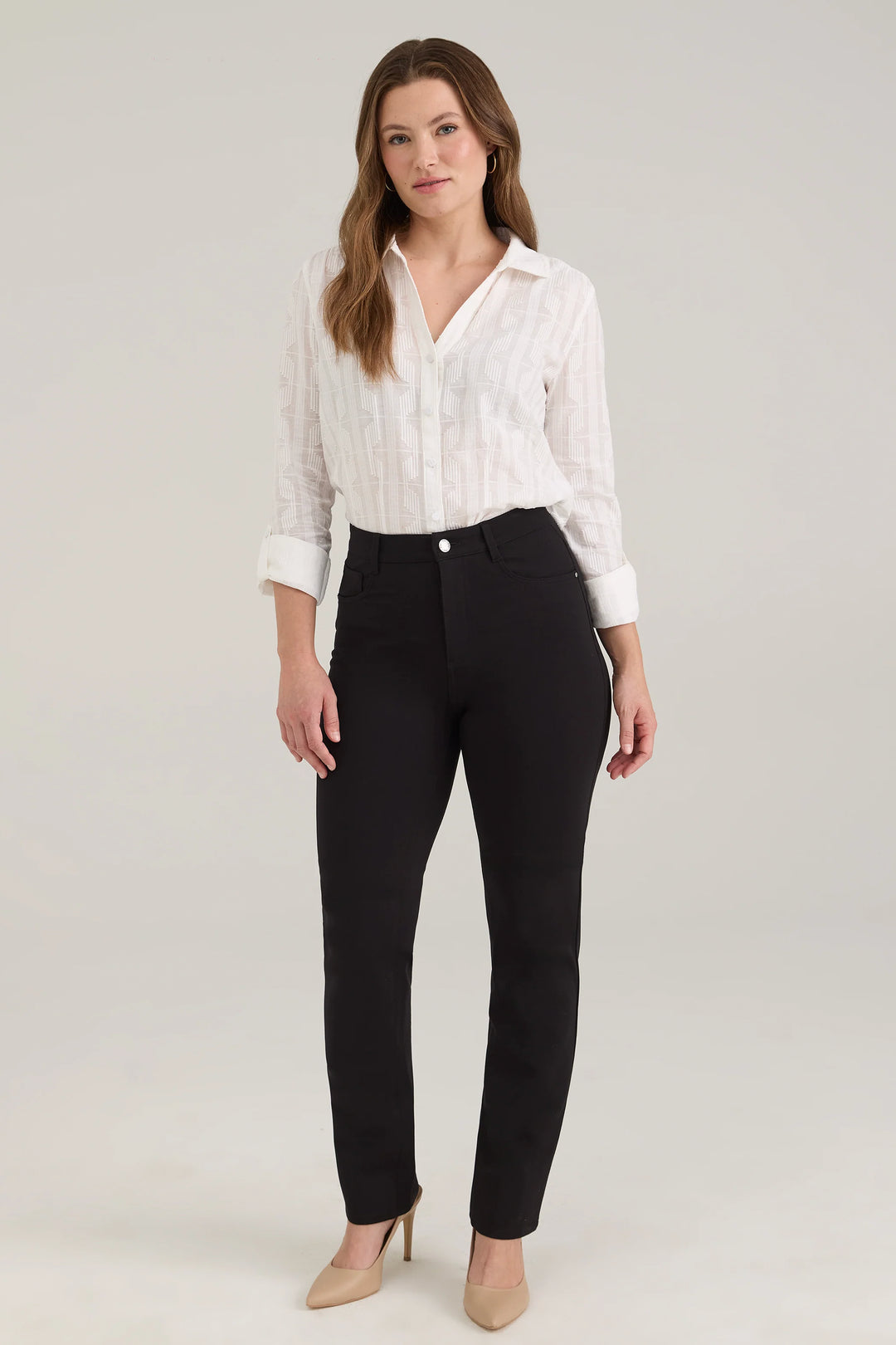 A woman modelling a white blouse and black pants standing in front of a light beige background. 