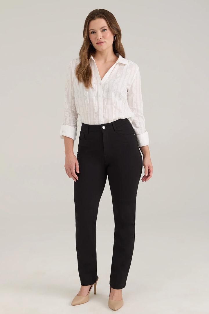 A woman modelling a white blouse and black pants standing in front of a light beige background. 