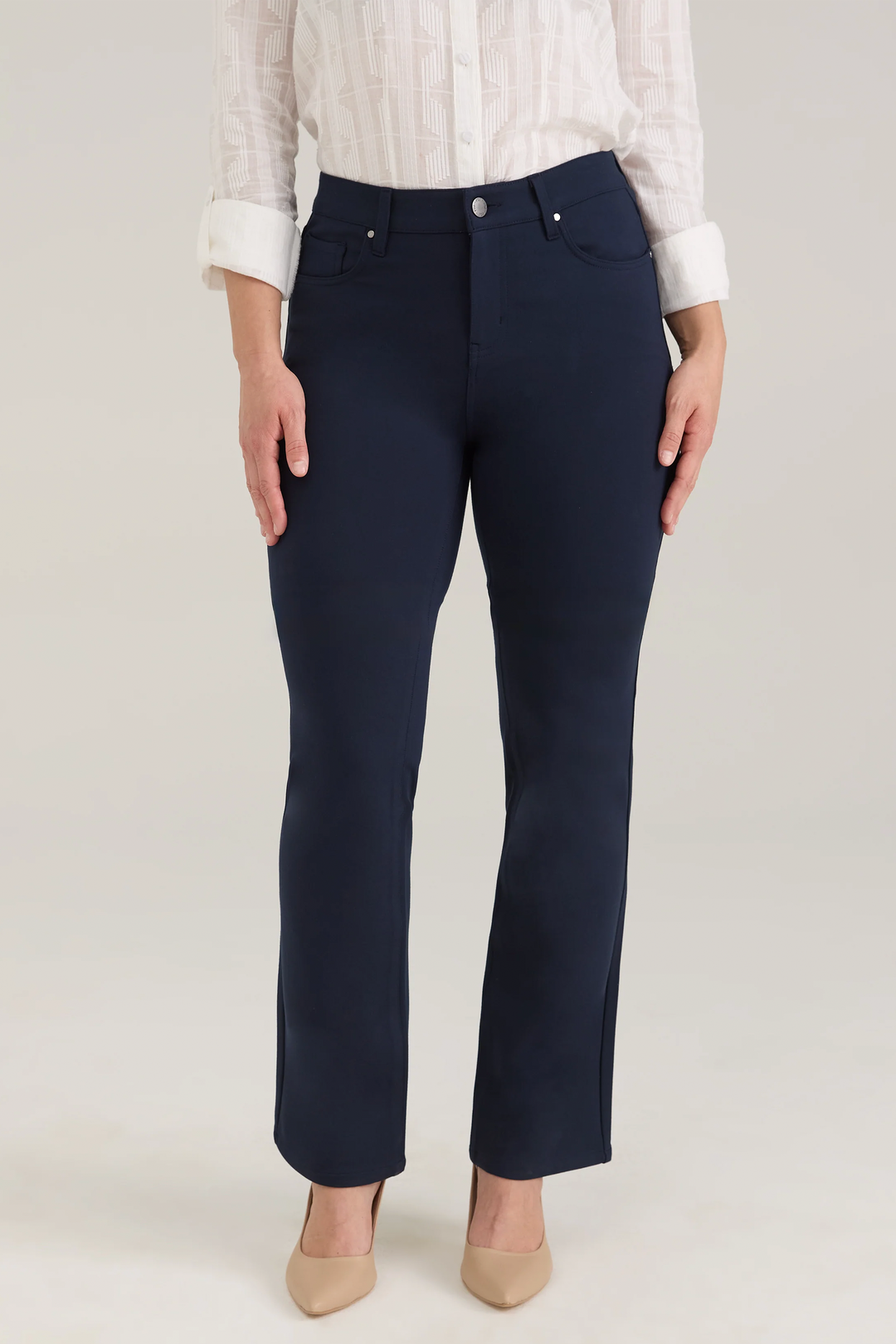 A woman modelling a white blouse and navy pants standing in front of a light beige background. 